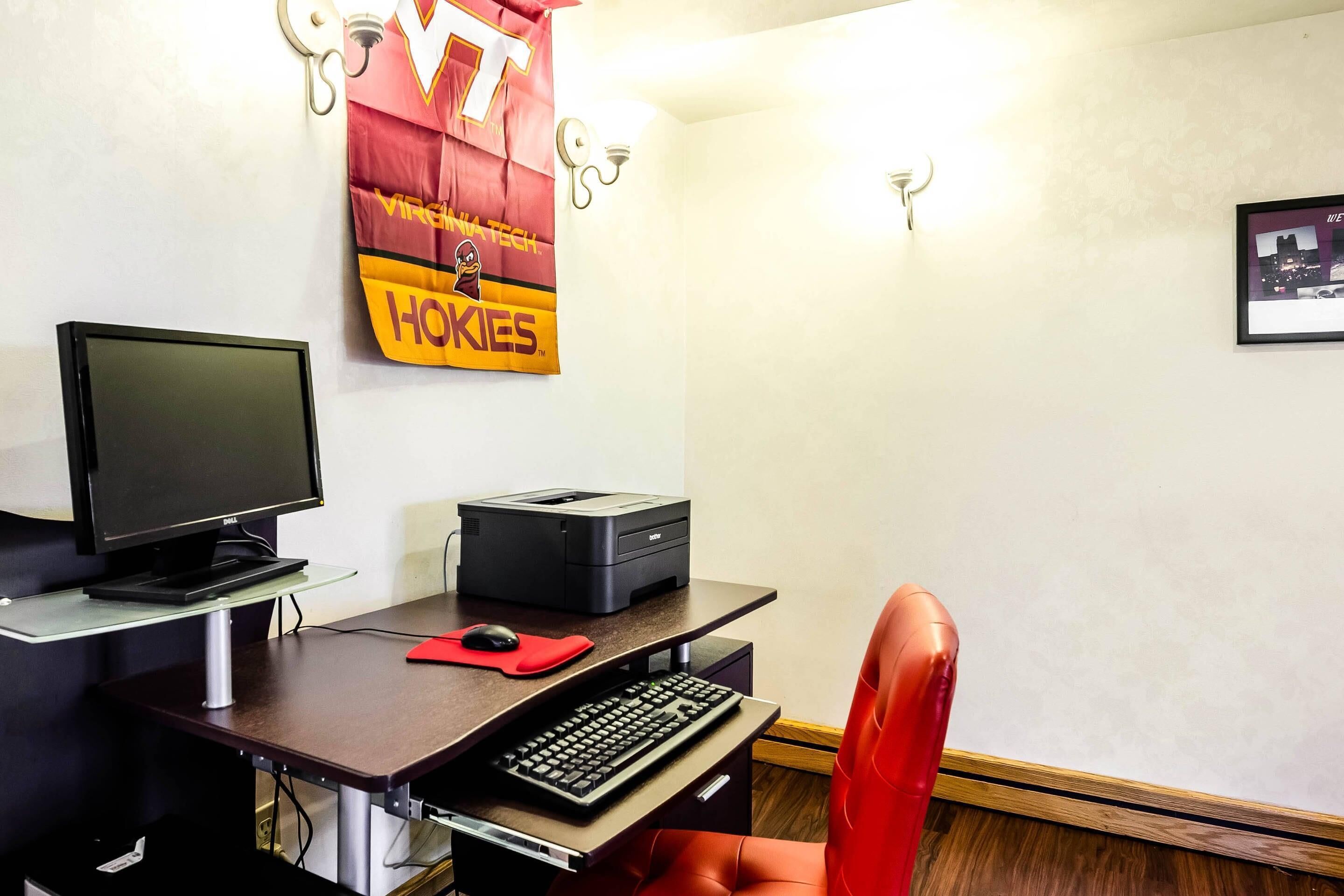 Une pièce comprenant un bureau, un ordinateur, une imprimante et une chaise rouge.