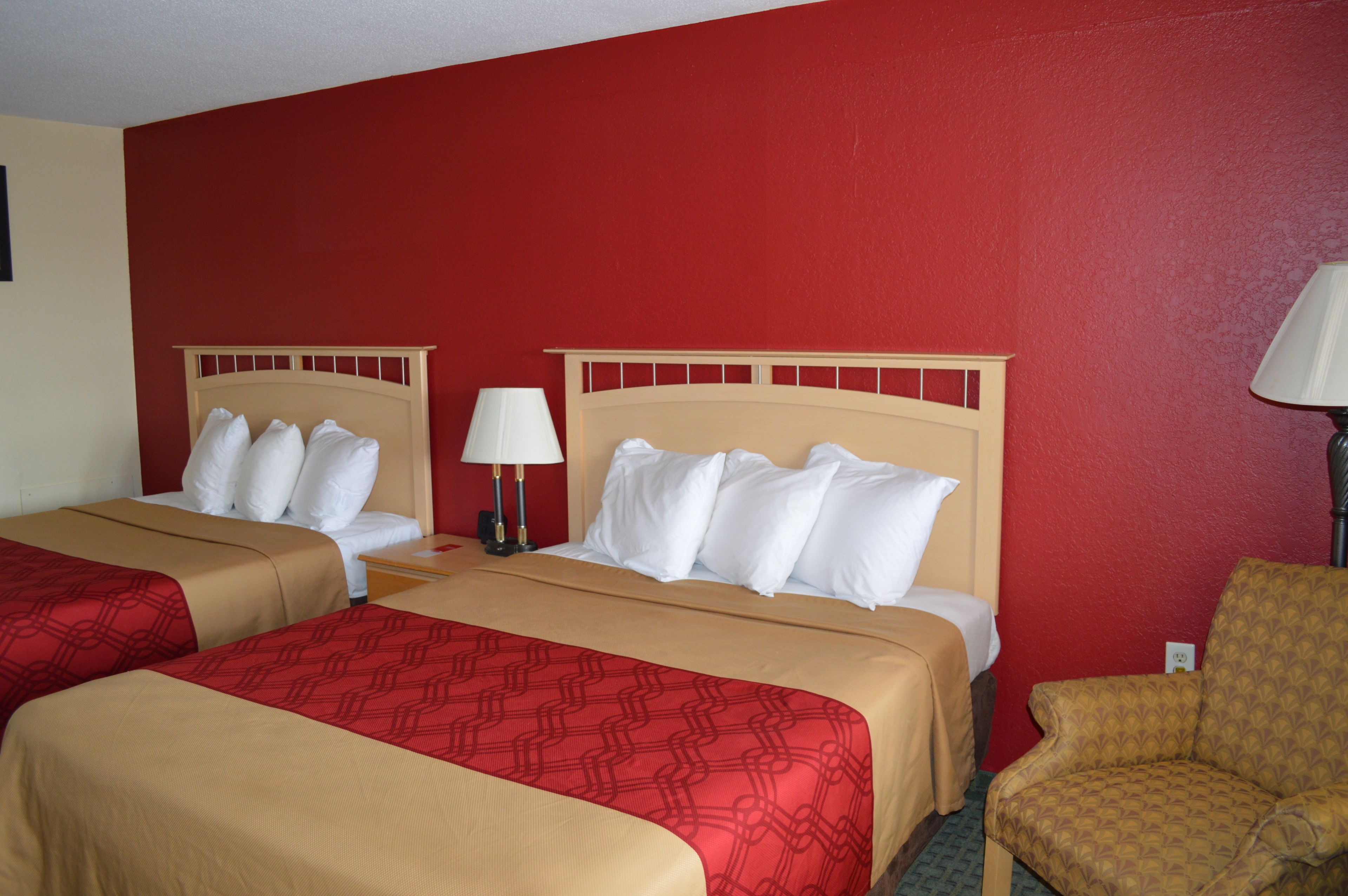 A hotel room with two beds, red walls, and a single armchair.