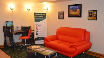 A hotel lobby with a desk, computer, and orange sofa. There are posters on the wall and a sign for 'The faster way to rewards'.