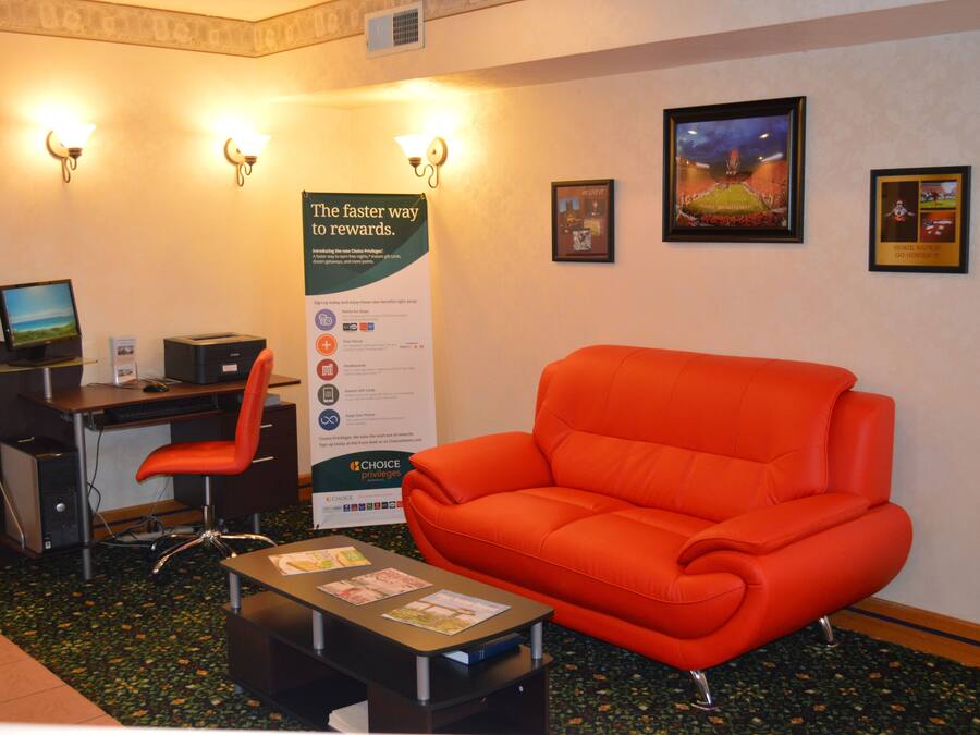 Un hall d’hôtel avec un comptoir, un ordinateur et un canapé orange. Des affiches sont accrochées au mur, et une enseigne indique : « La voie la plus rapide vers les récompenses ».