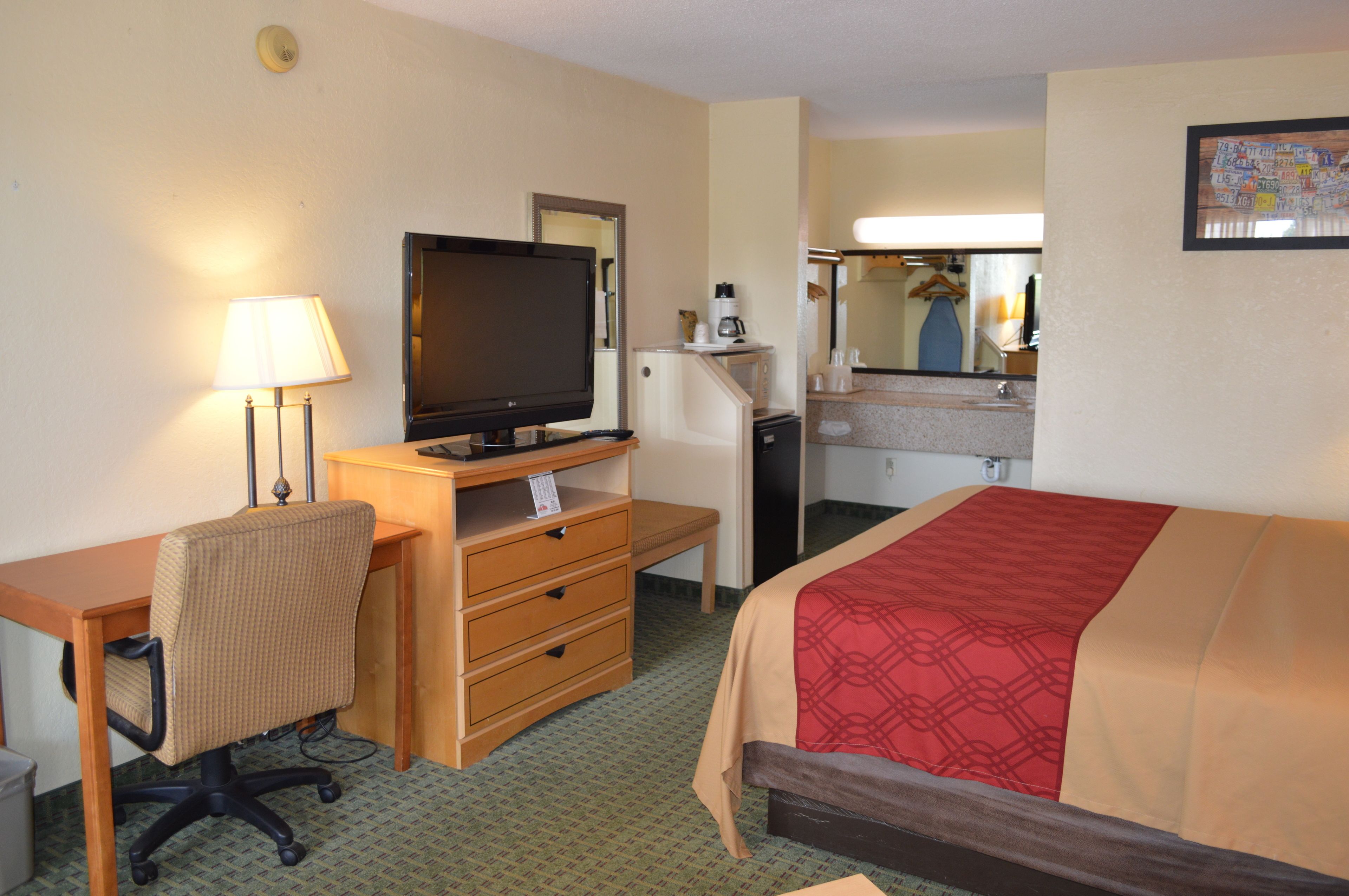 A hotel room with a bed, a desk with a computer, a television, a lamp, and a refrigerator.