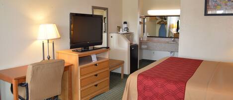 A hotel room with a bed, a desk with a computer, a television, a lamp, and a refrigerator.