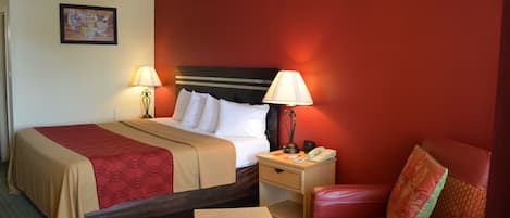 A hotel room with a bed, two bedside tables with lamps, a nightstand, a chair, and a small table.