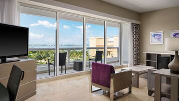 A modern hotel room with a large balcony, a flat-screen TV, a comfortable seating area, and a view of the city skyline.