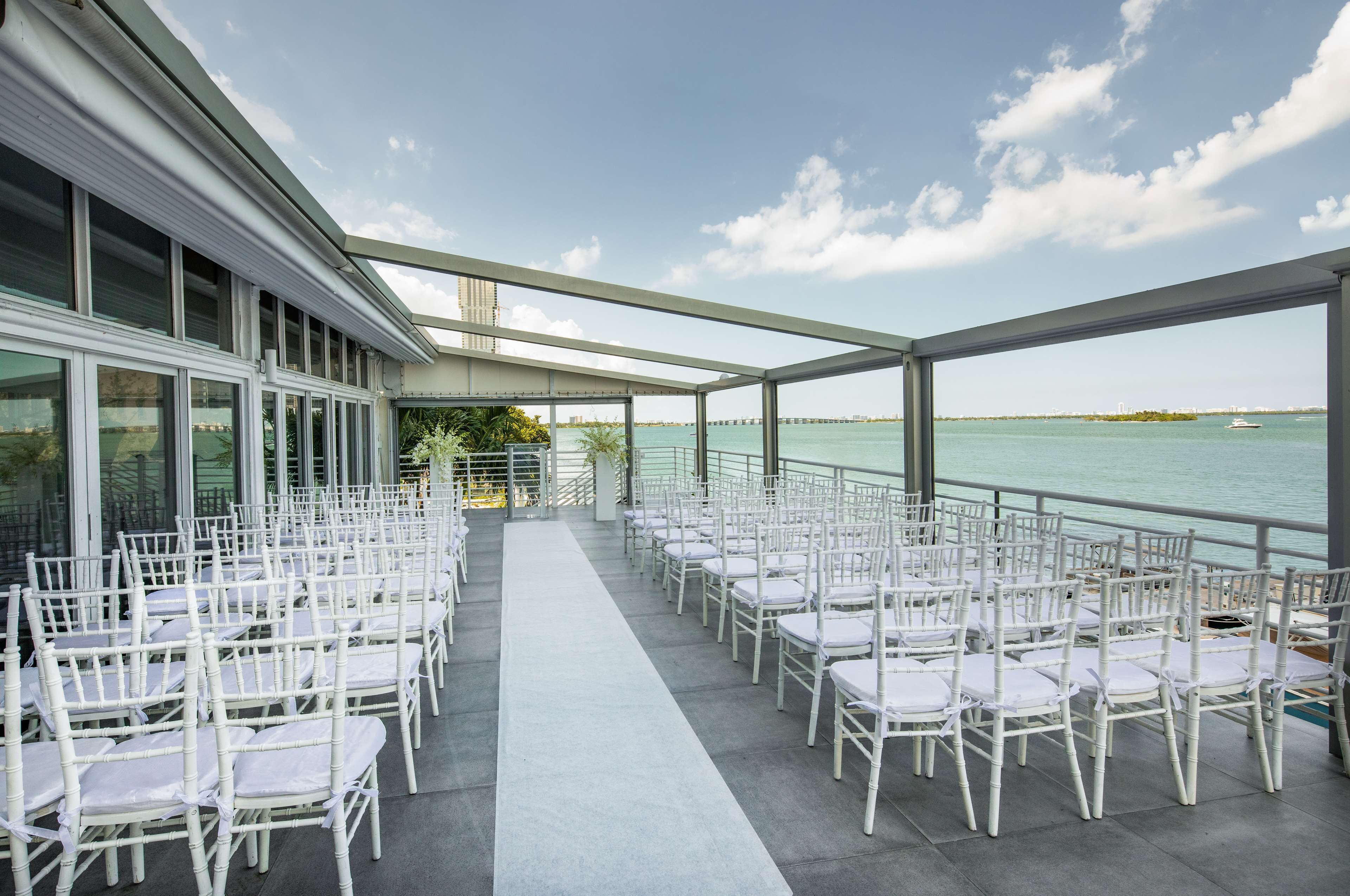 A covered outdoor area with rows of white chairs and a view of the water.