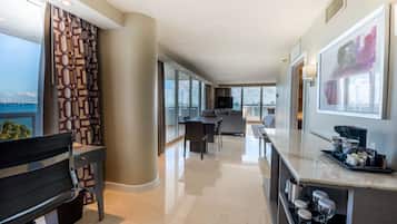 A modern hotel room with a large window, a dining area, and a kitchen.