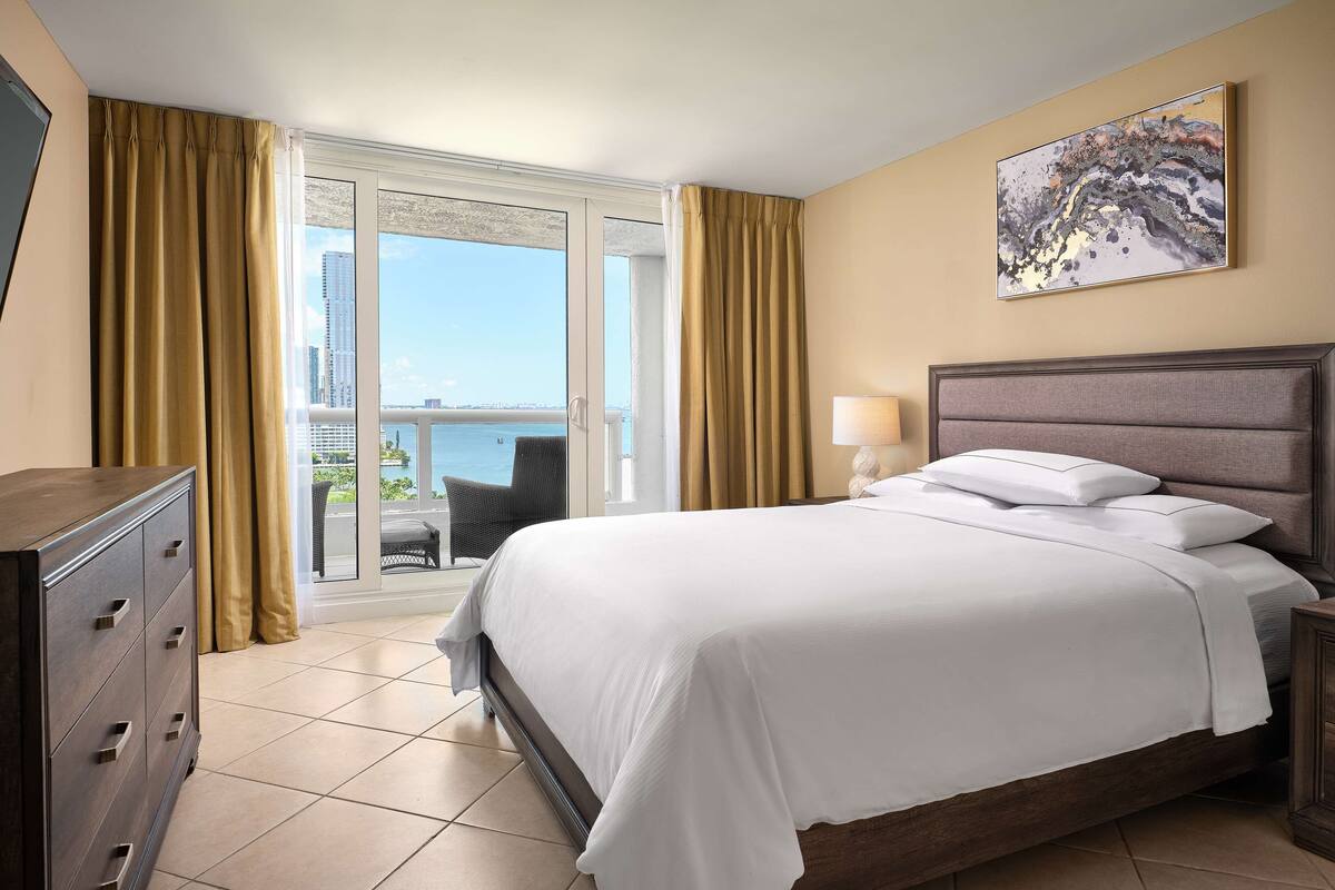 A hotel room with a bed, a dresser, a lamp, and a painting on the wall.