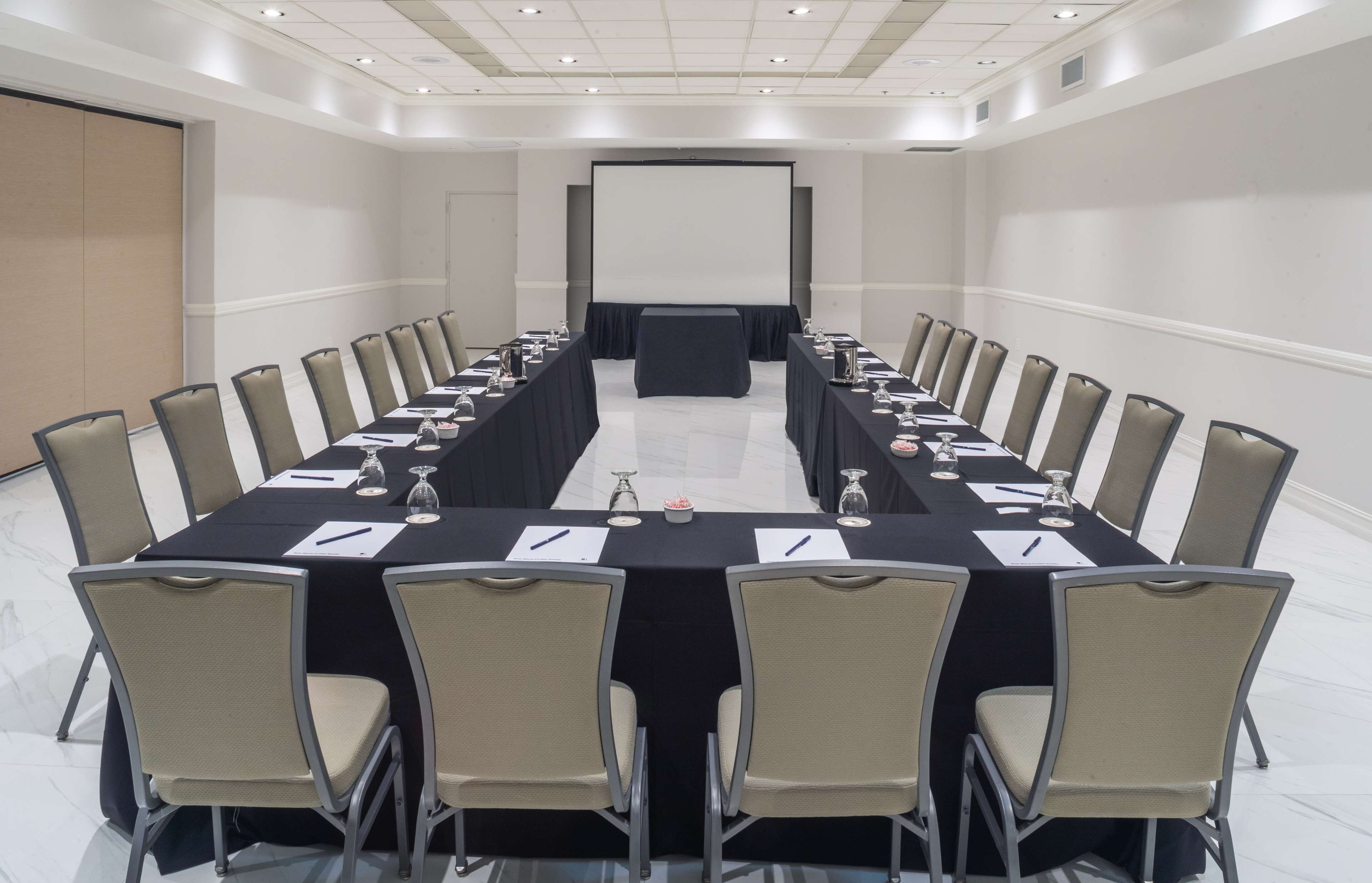 Uma sala de conferências com uma mesa comprida, cadeiras, tela de projetor e quadro branco.