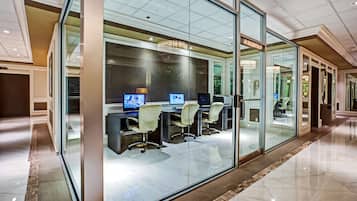 A modern office space with glass walls, multiple computer workstations, and a chandelier.