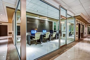 A modern office space with glass walls, multiple computer workstations, and a chandelier. - DoubleTree by Hilton Grand Hotel Biscayne Bay (Miami)