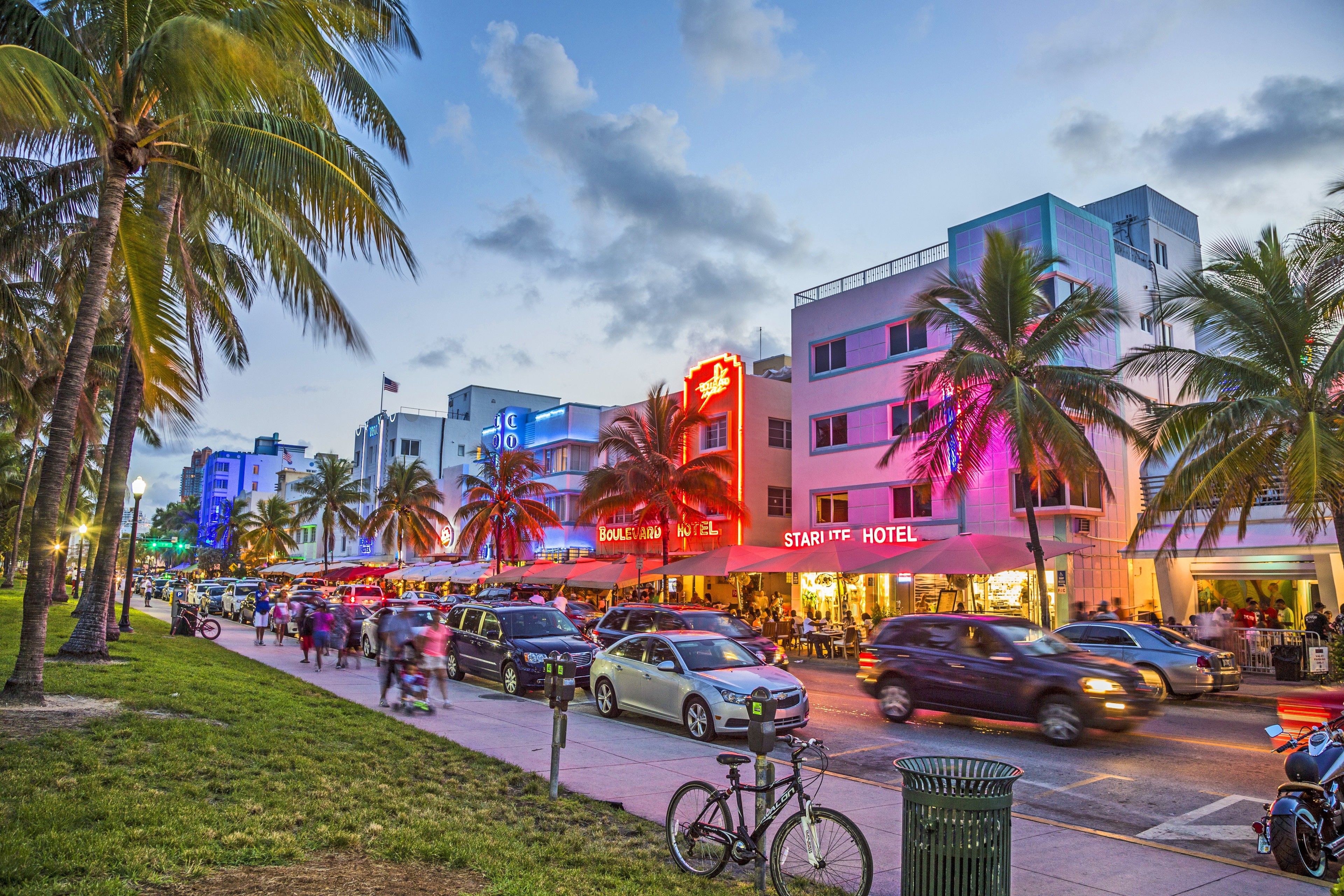 A hotel with a neon sign, palm trees, and a busy street with cars and pedestrians.