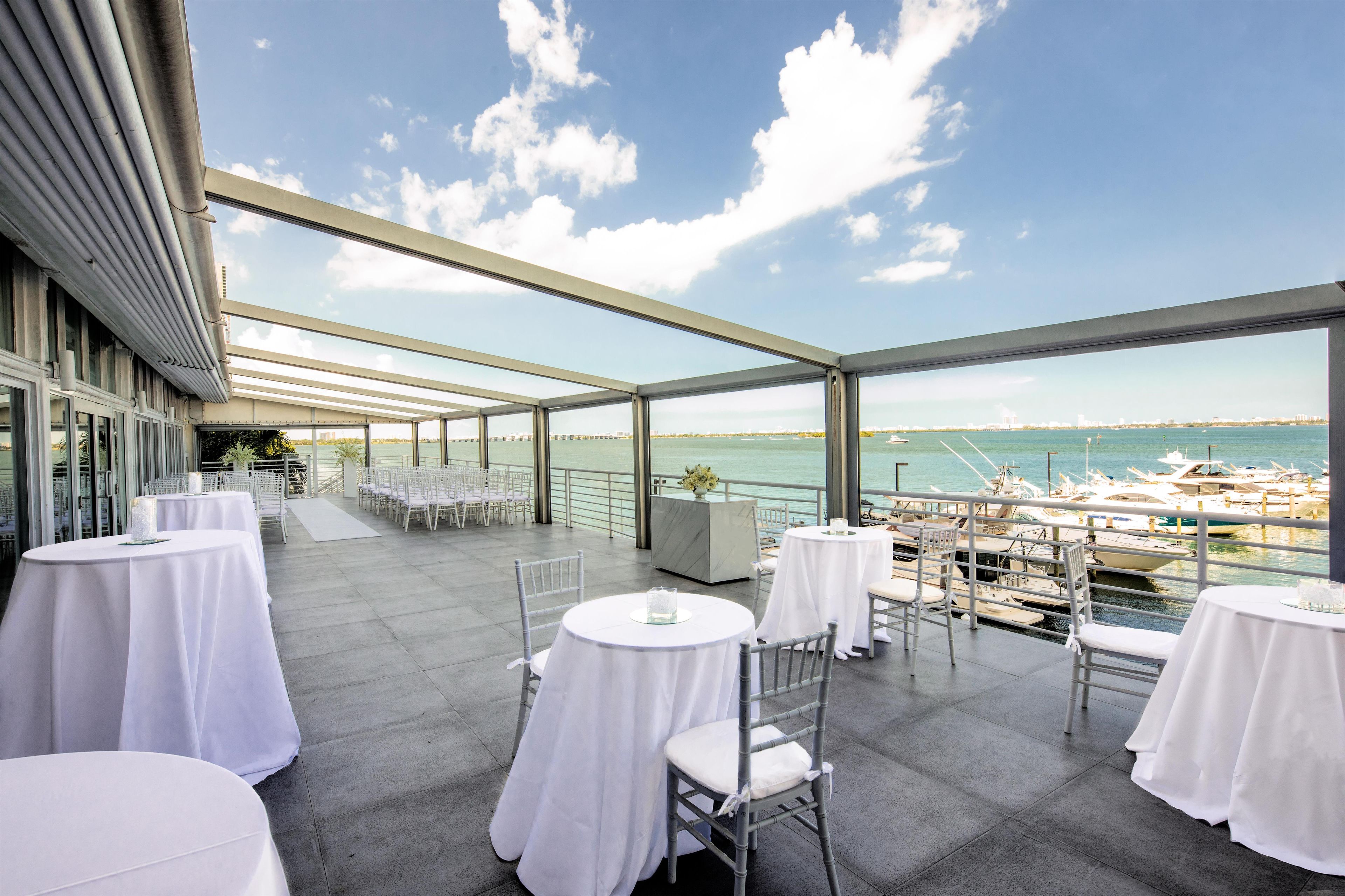 Une terrasse avec des tables et des chaises, donnant sur une marina où sont amarrés des bateaux.