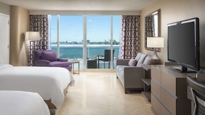 A hotel room with two beds, a sofa, a TV, and a view of the sea and city skyline. - DoubleTree by Hilton Grand Hotel Biscayne Bay (Miami)