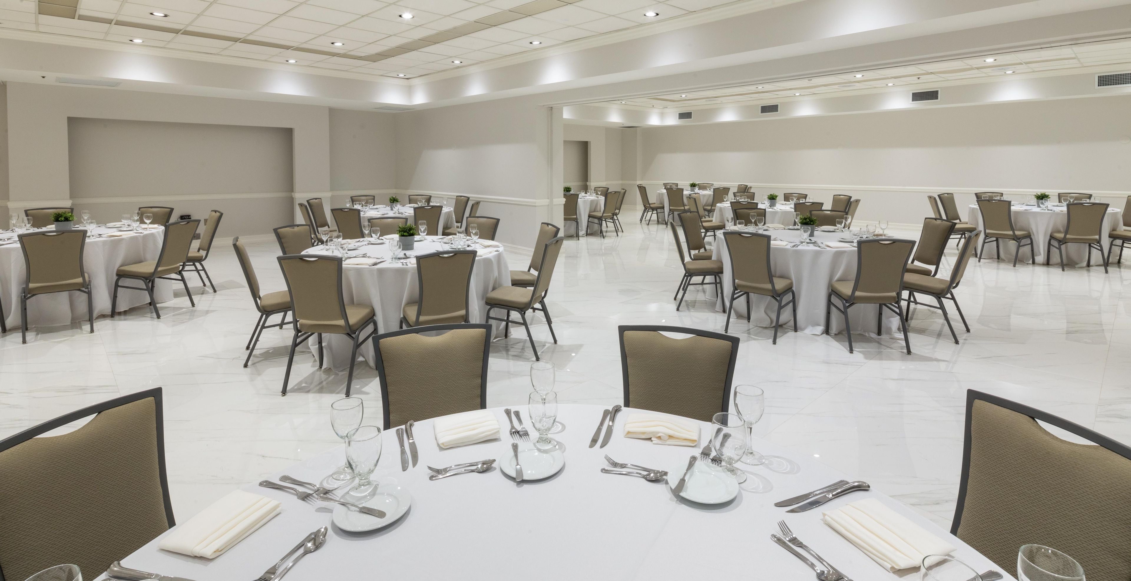 Un amplio salón de banquetes con varias mesas redondas dispuestas para cenar, cada una con sillas y una vajilla.