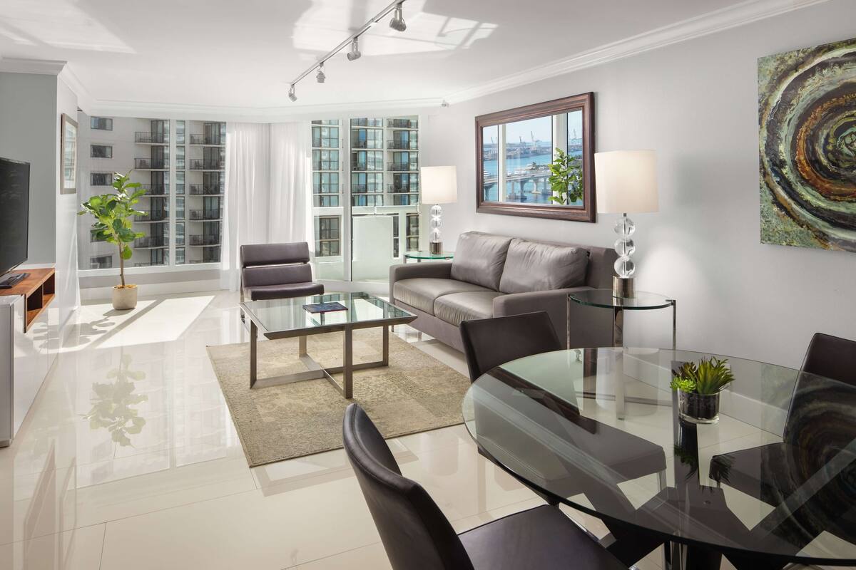 A modern living room with a glass coffee table, leather sofa, and a dining table with chairs.