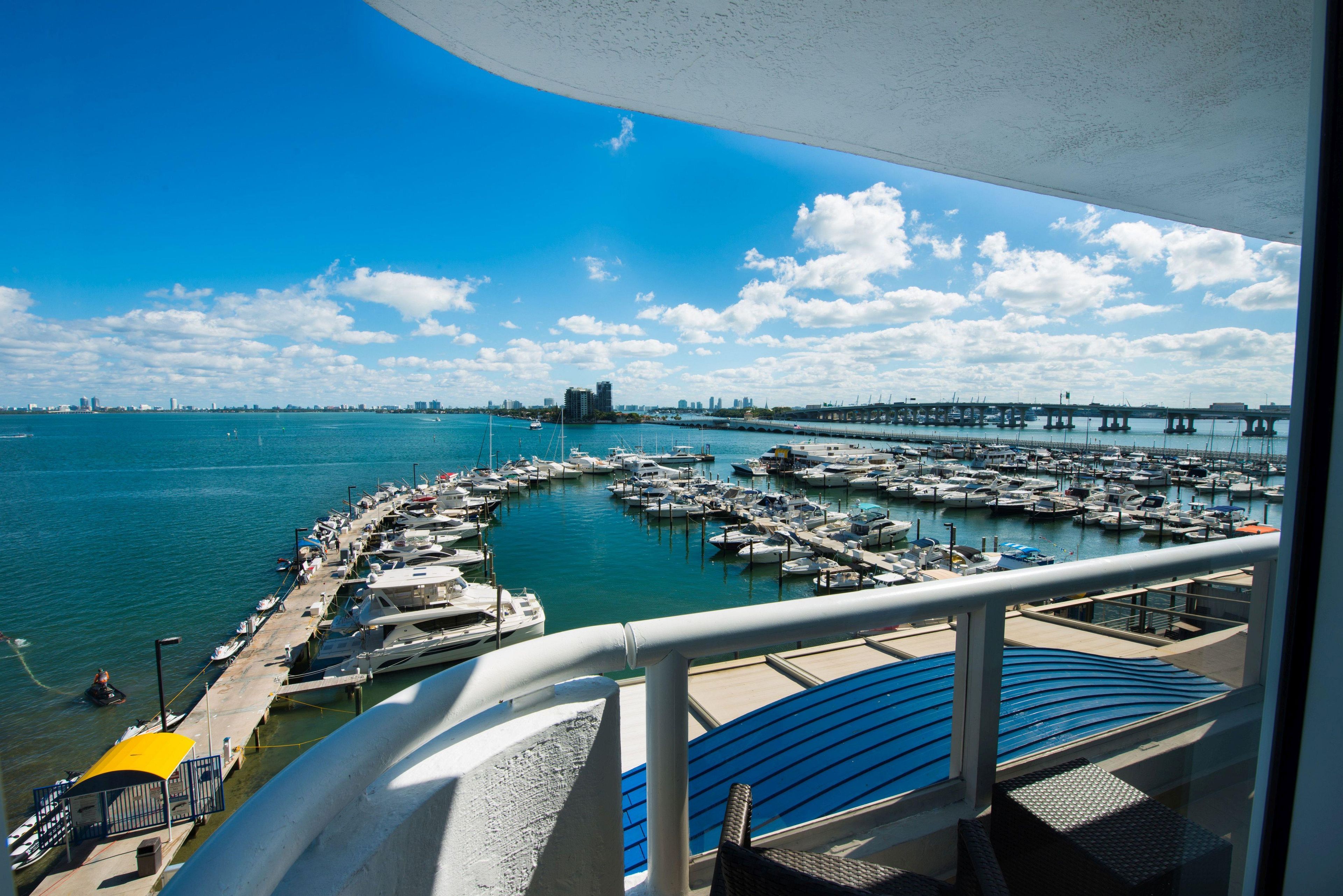 A marina with boats docked, a bridge in the background, and a clear sky.