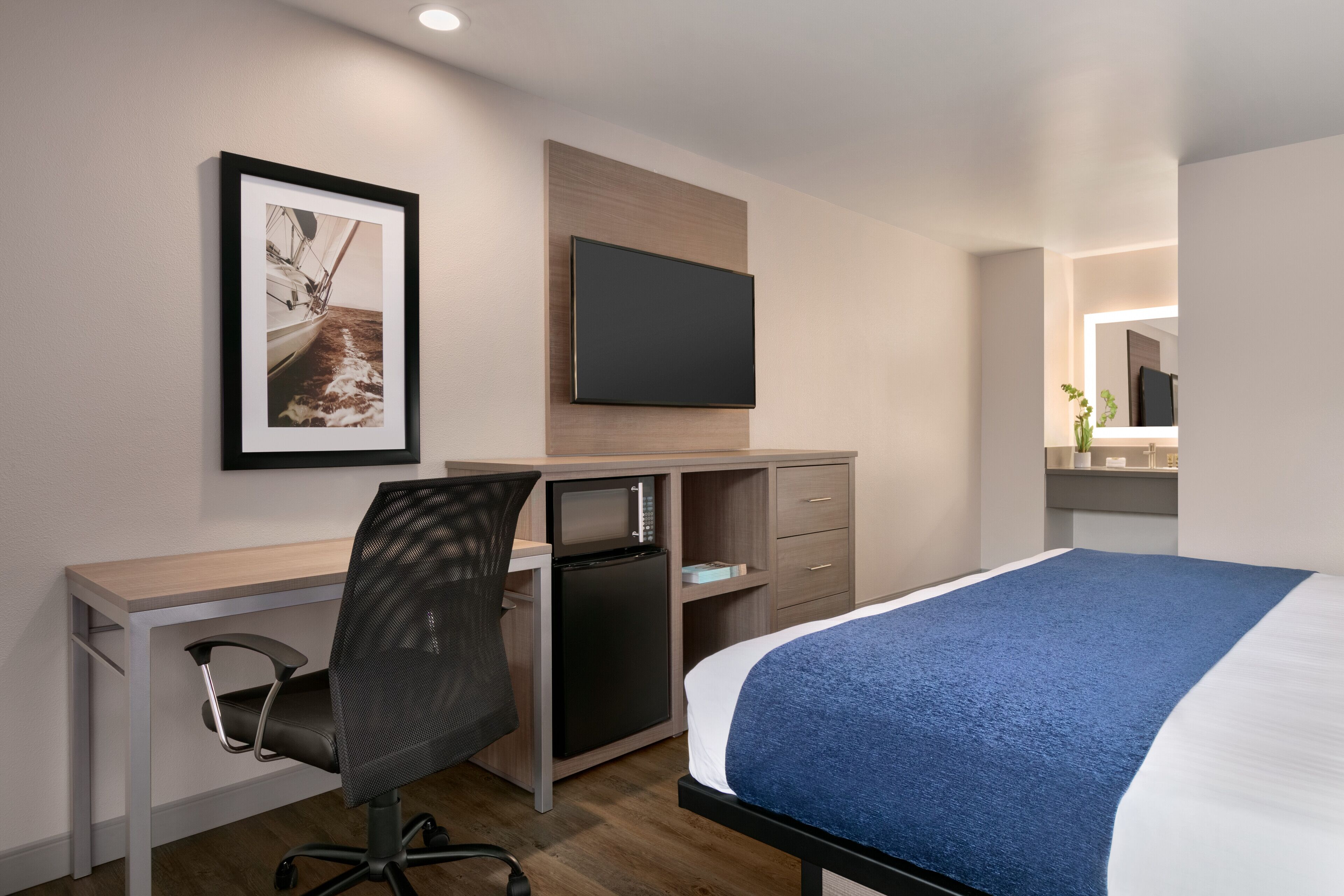 Una habitación de hotel moderna con cama, escritorio, silla, televisor y un cuadro enmarcado en la pared.