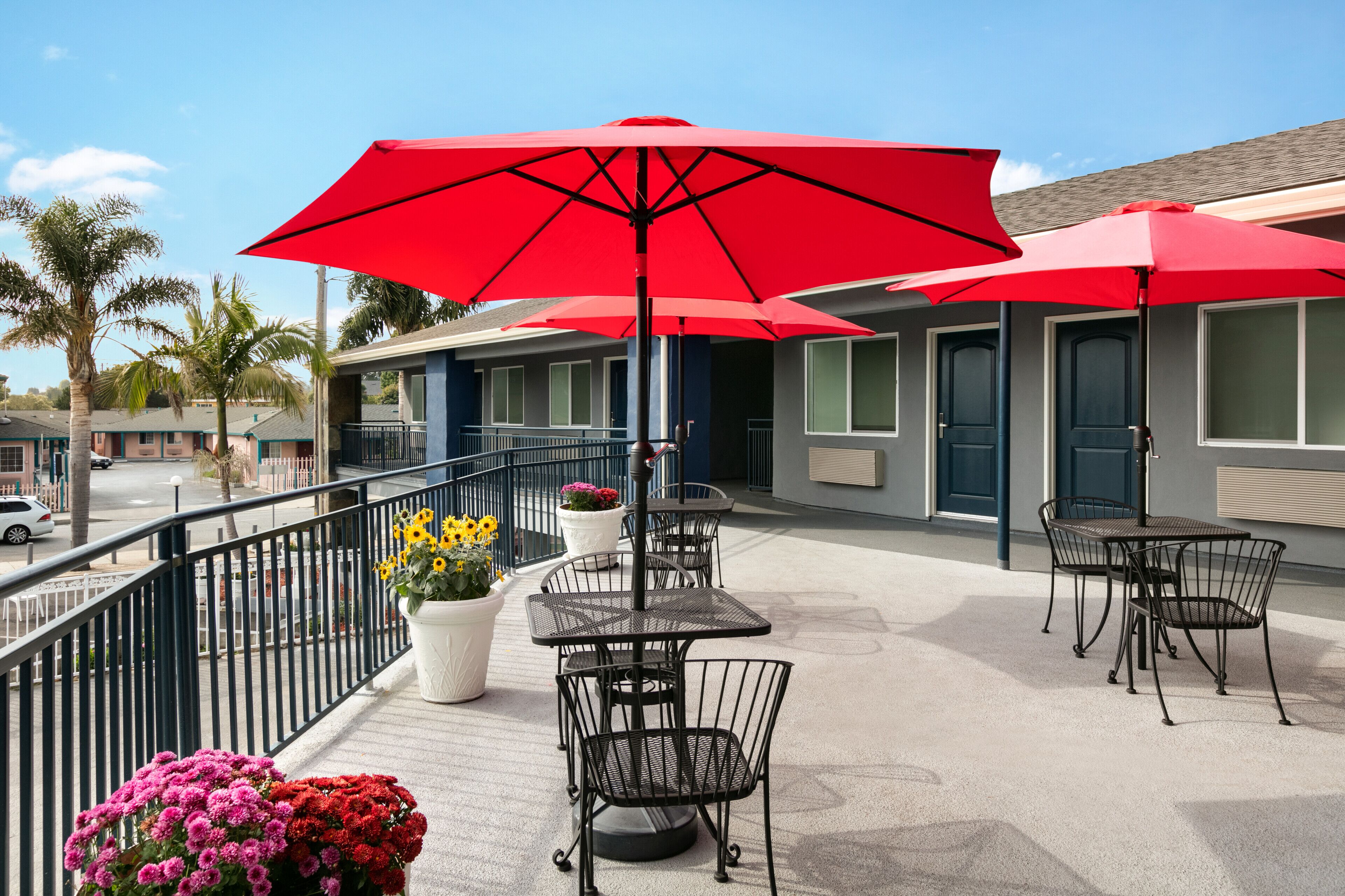 A rooftop patio with outdoor seating, red umbrellas, and potted flowers.