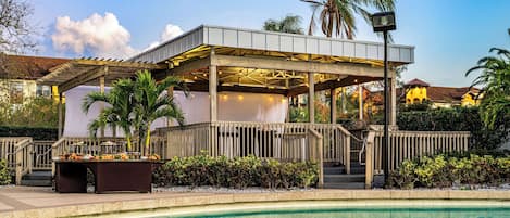 Un espacio al aire libre cubierto con piscina, terraza de madera y palmeras.