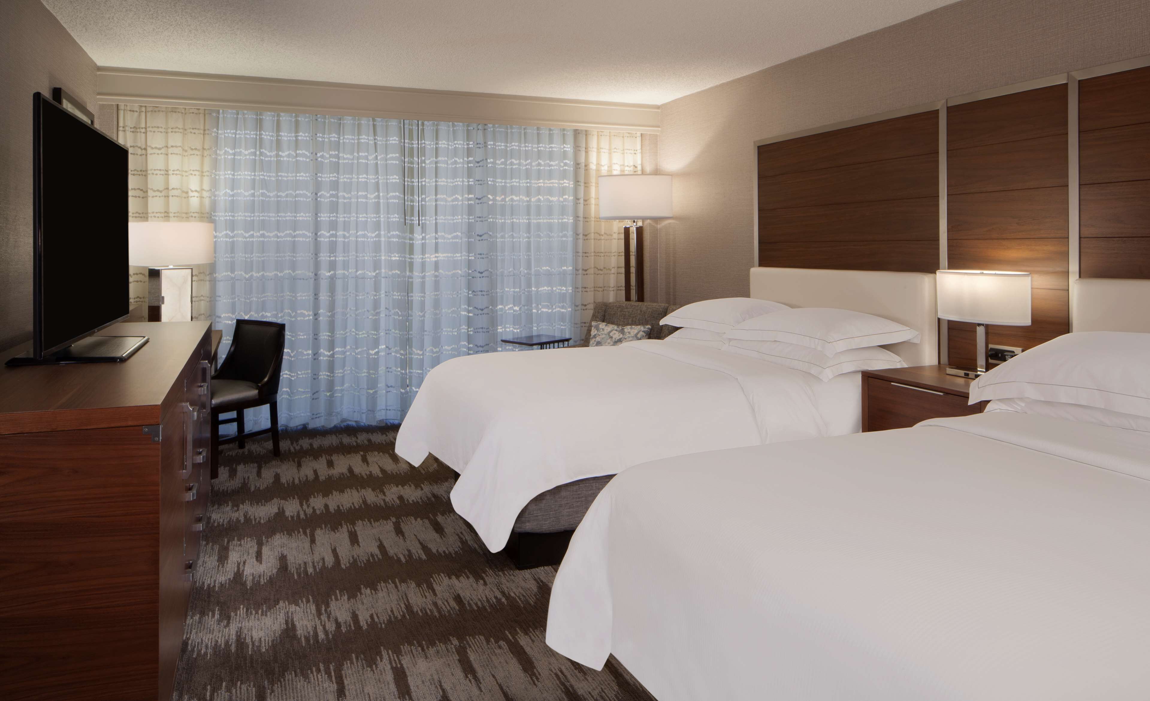 A hotel room with two beds, a desk with a TV, and a chair.