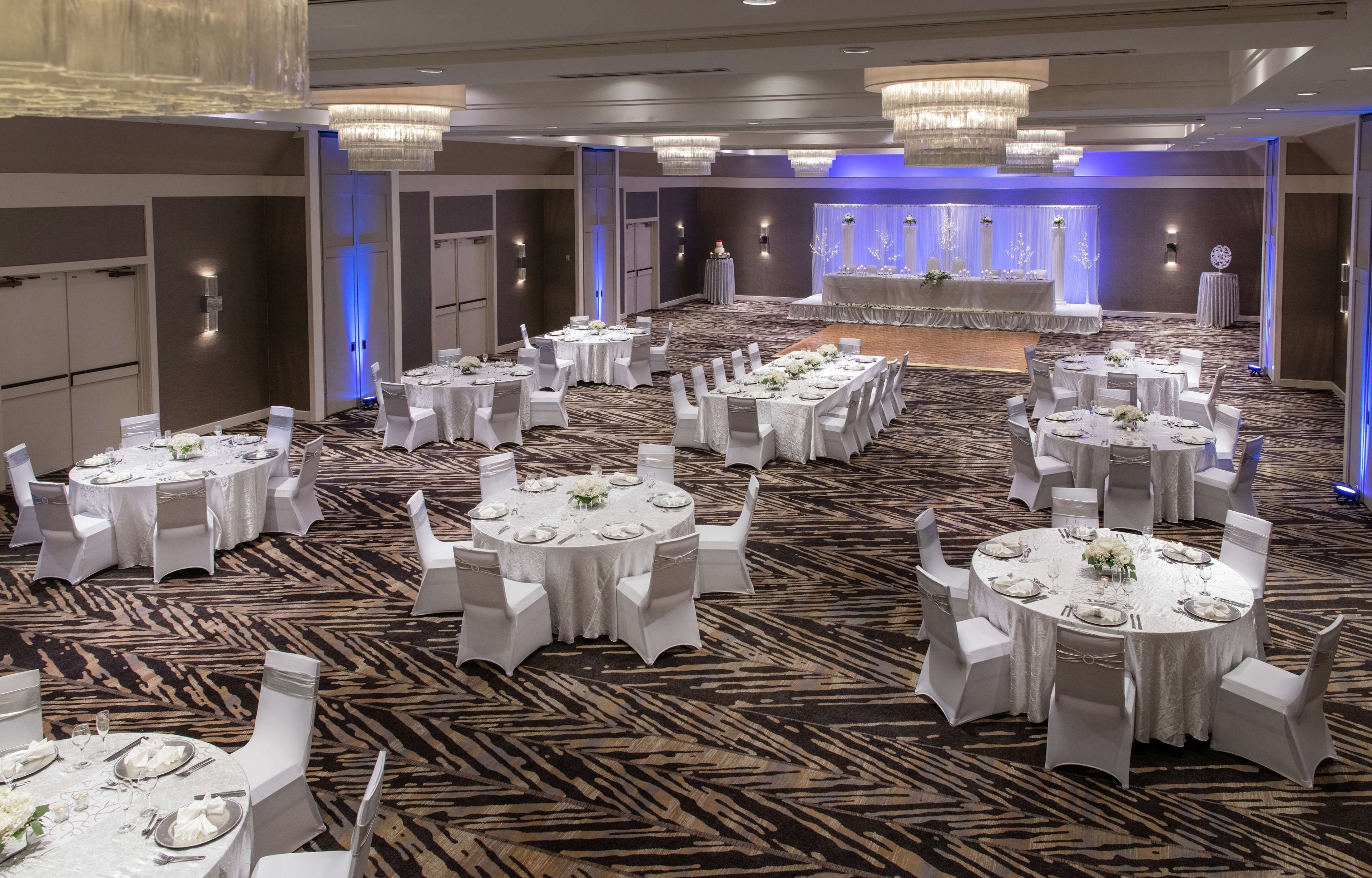 A banquet hall with multiple round tables, each set with white tablecloths, chairs, and centerpieces.