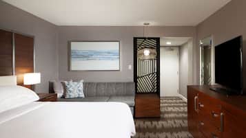 A hotel room with a bed, a sofa, a TV, a dresser, and a painting on the wall.