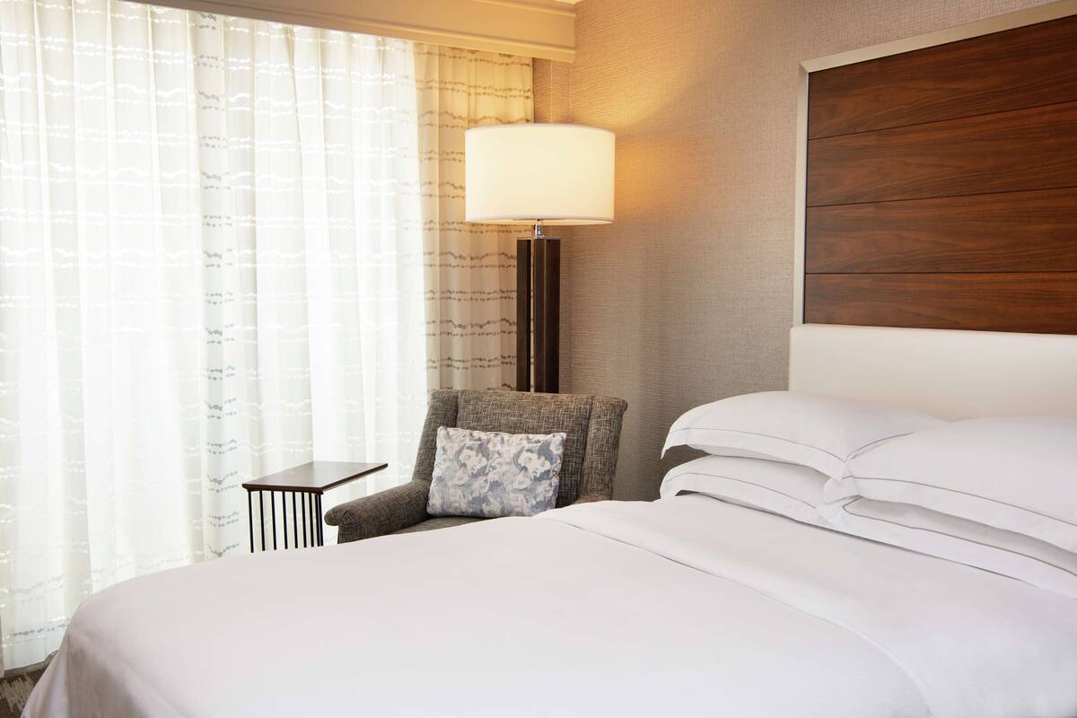 A hotel room with a large bed, a nightstand, a lamp, and a chair.