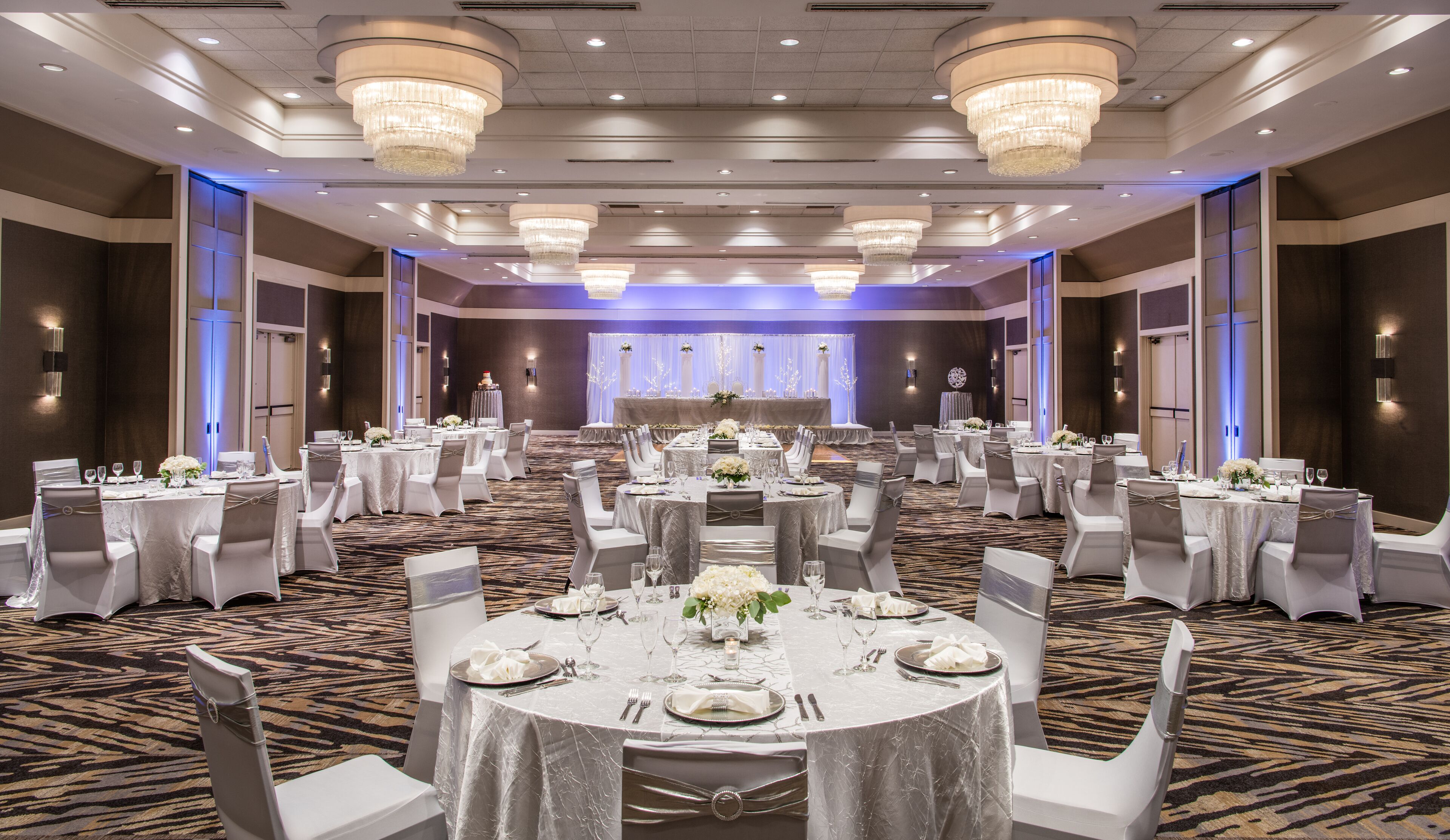 Une salle de banquet avec des tables rondes, des chaises blanches et des lustres.