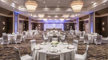 Une salle de banquet avec des tables rondes, des chaises blanches et des lustres.