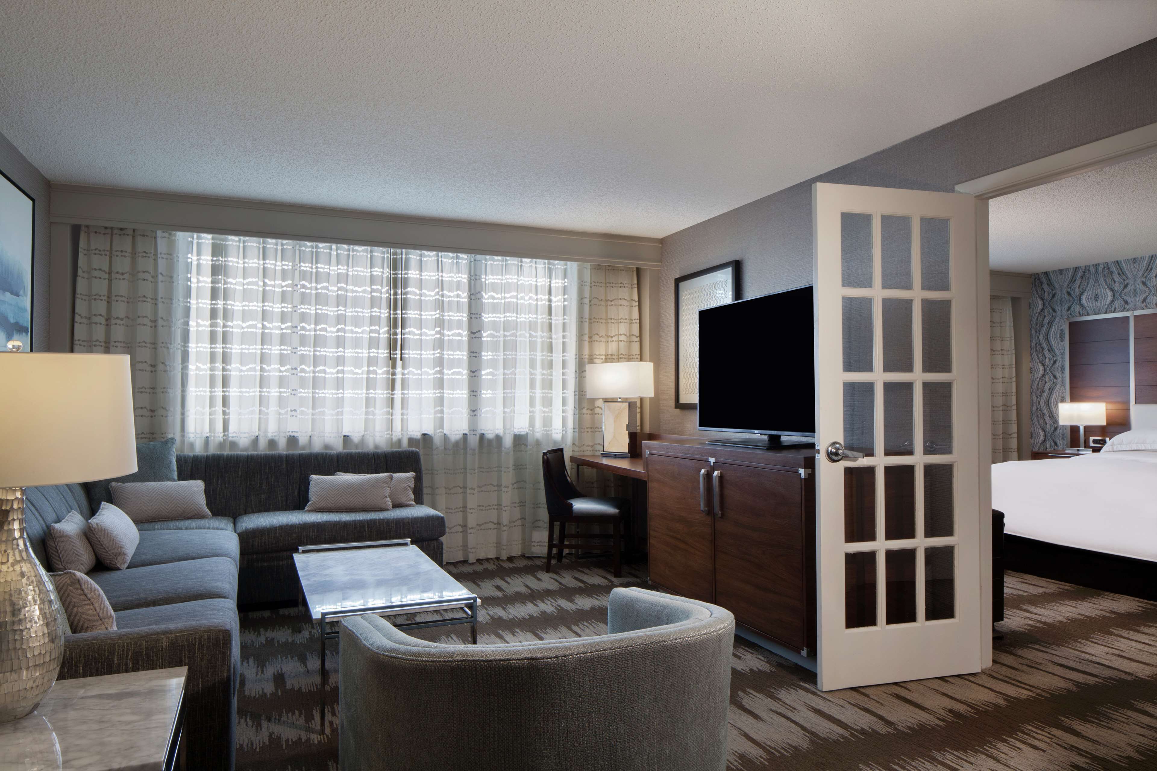 A hotel room with a sofa, armchair, TV, desk, and a bed.