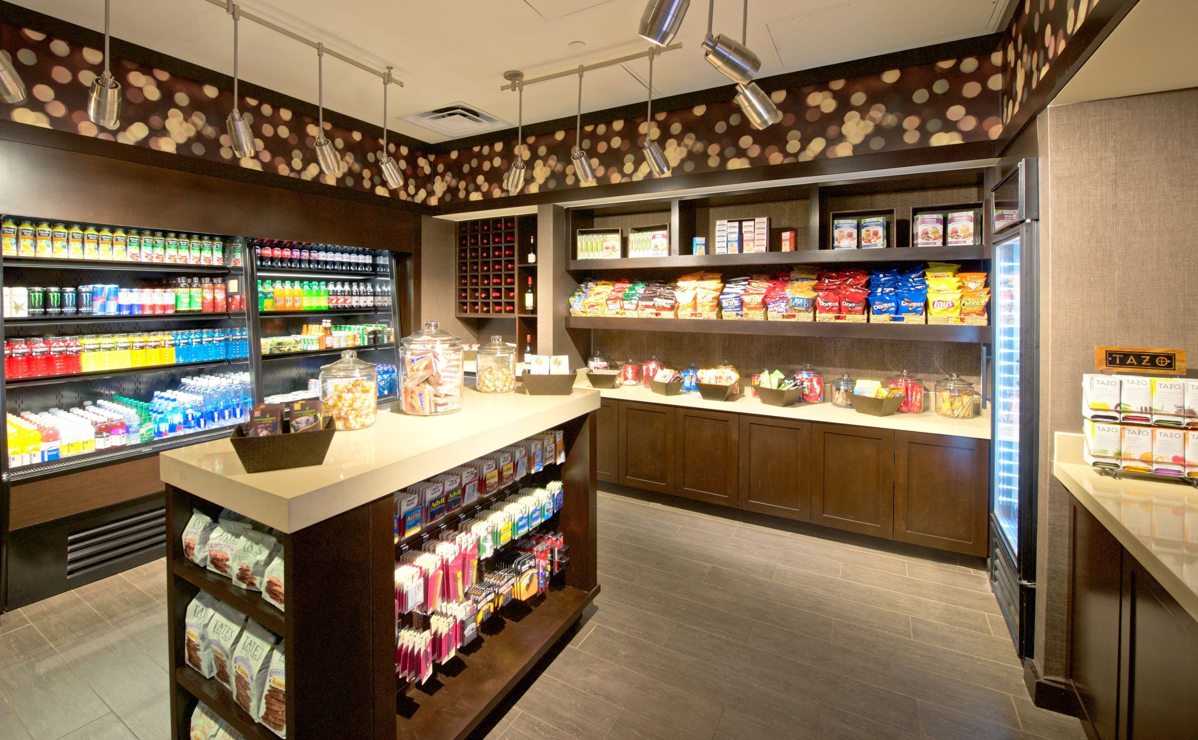 A well-lit snack bar with a variety of beverages and snacks, including a refrigerated section with sodas and juices, and shelves stocked with chips, cookies, and other packaged foods.