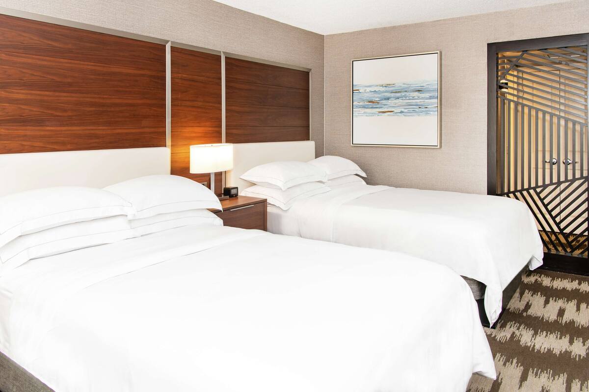 A hotel room with two beds, a nightstand, a lamp, a framed picture, and a patterned rug.