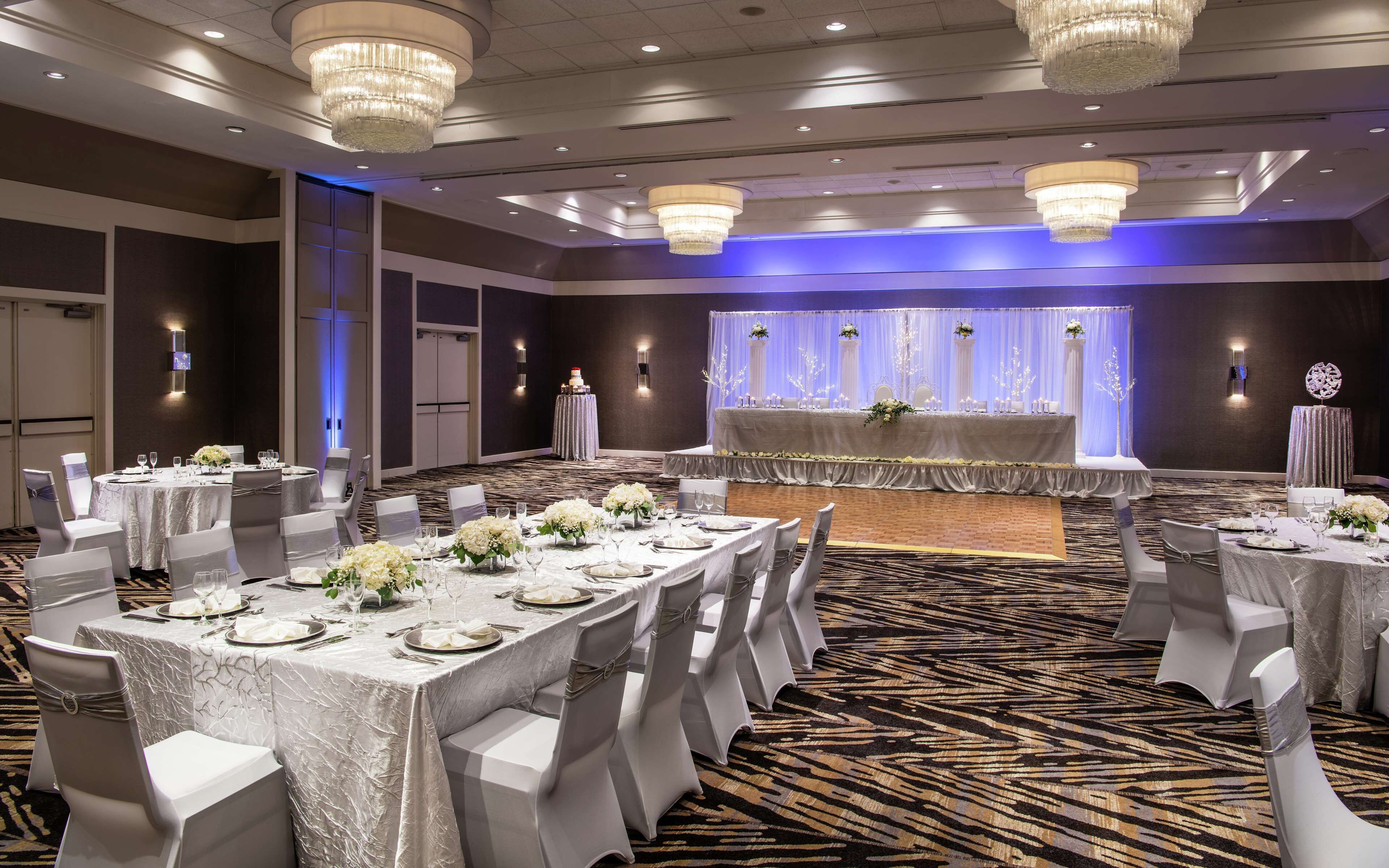 A banquet hall with round tables, white chairs, and chandeliers.