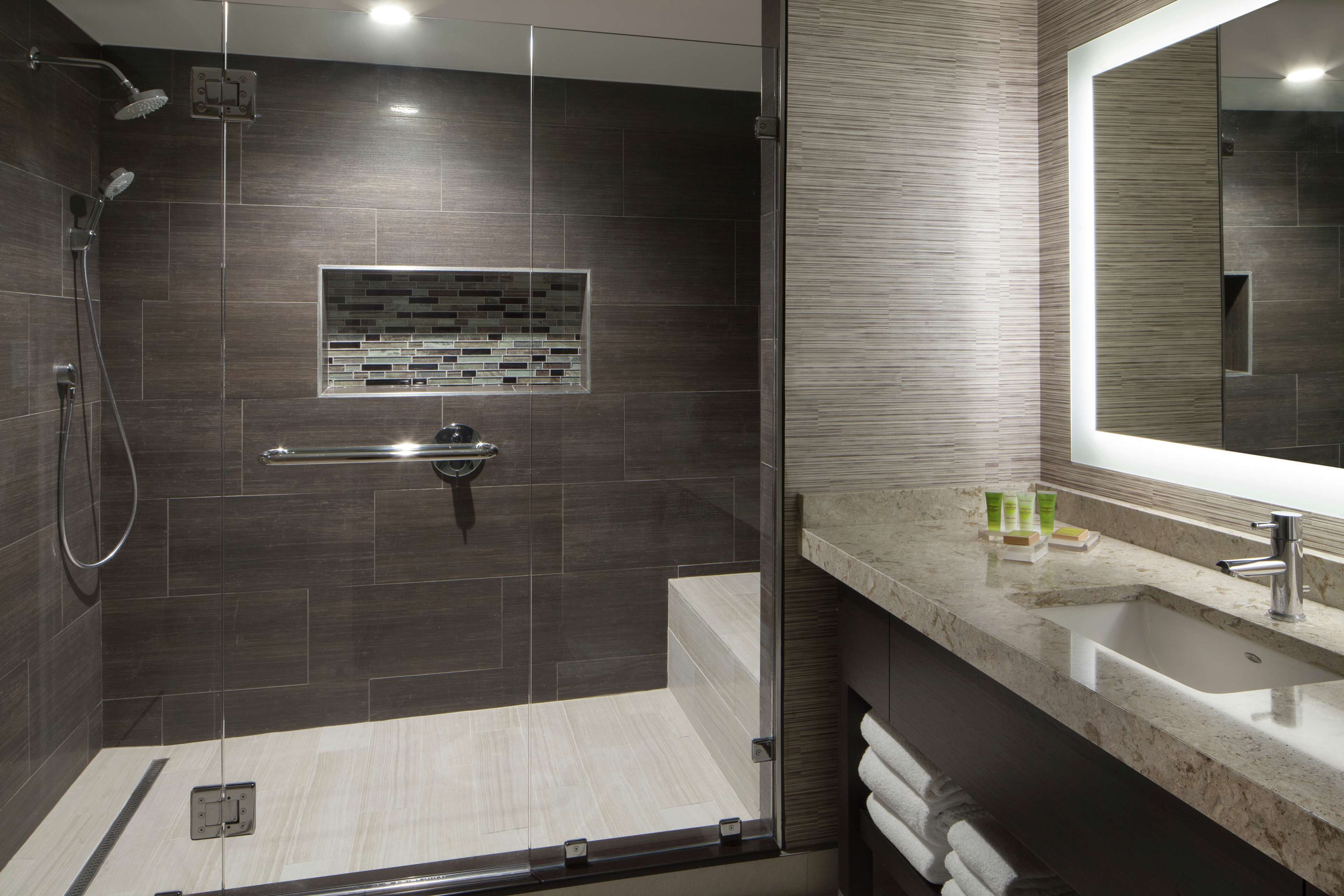 A modern bathroom with a glass-enclosed shower, a large mirror, and a marble countertop.