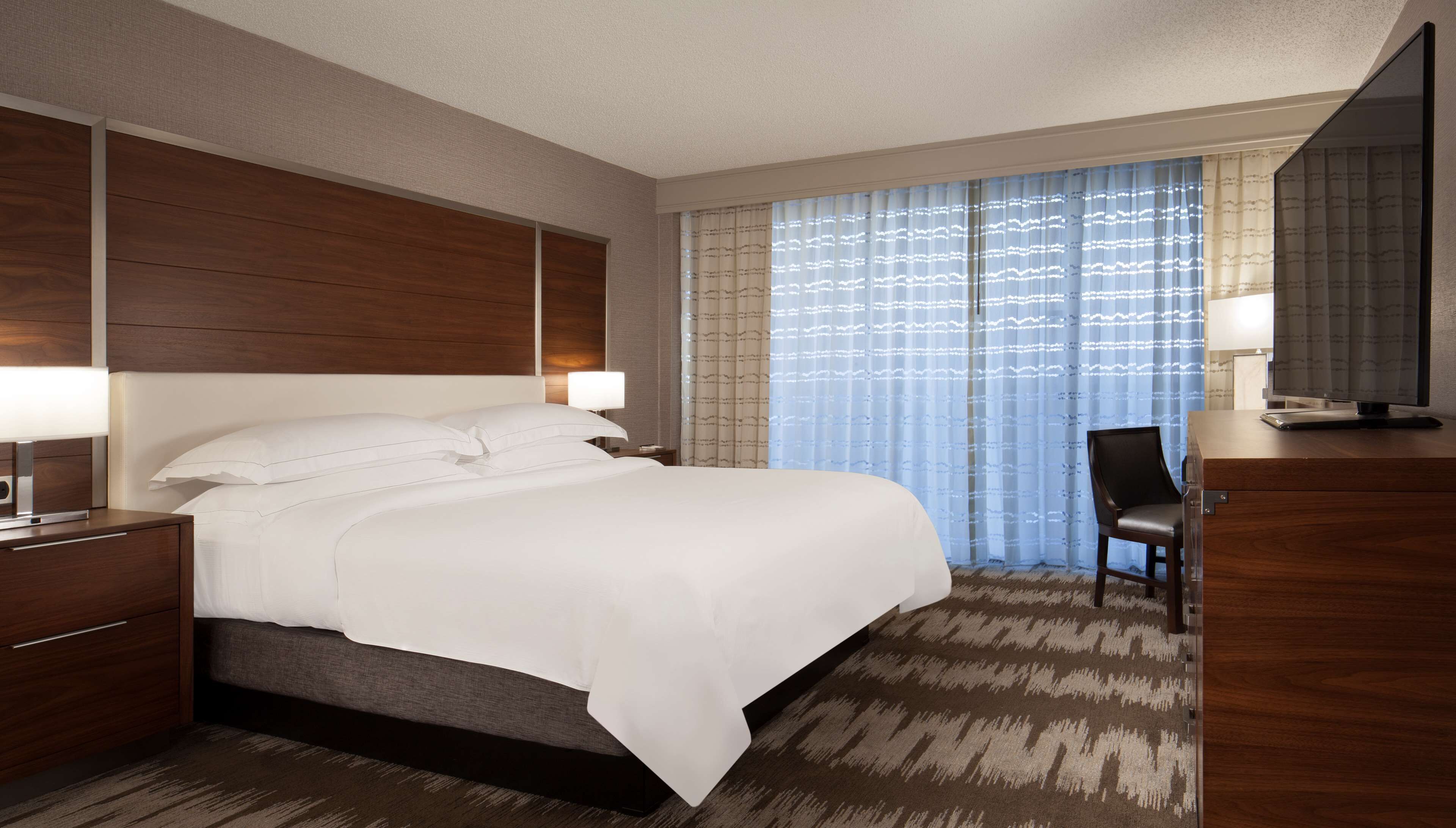 A hotel room with a large bed, a desk with a computer, and a chair.