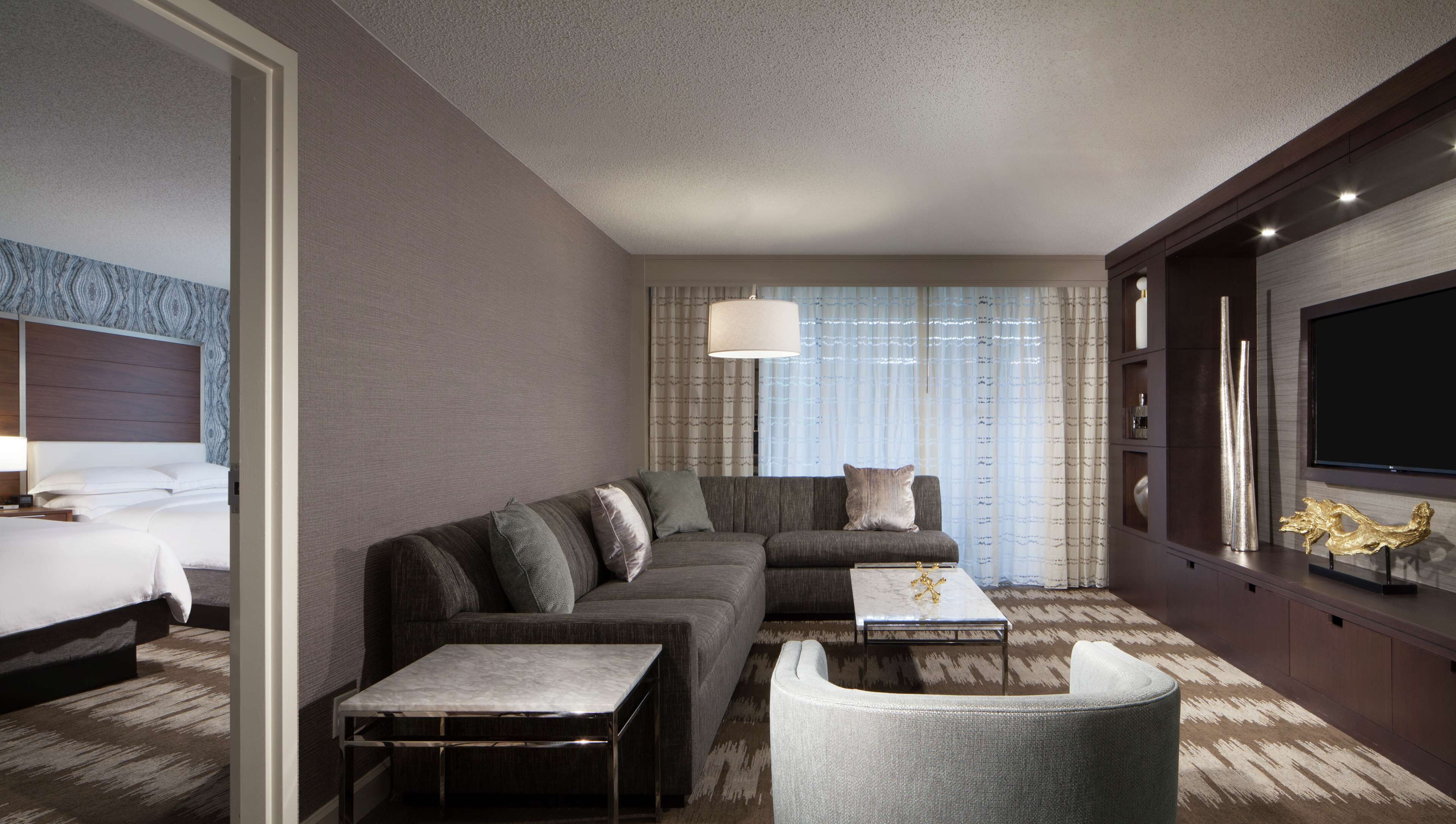 A modern hotel room with a large bed, a sofa, a coffee table, and a TV.