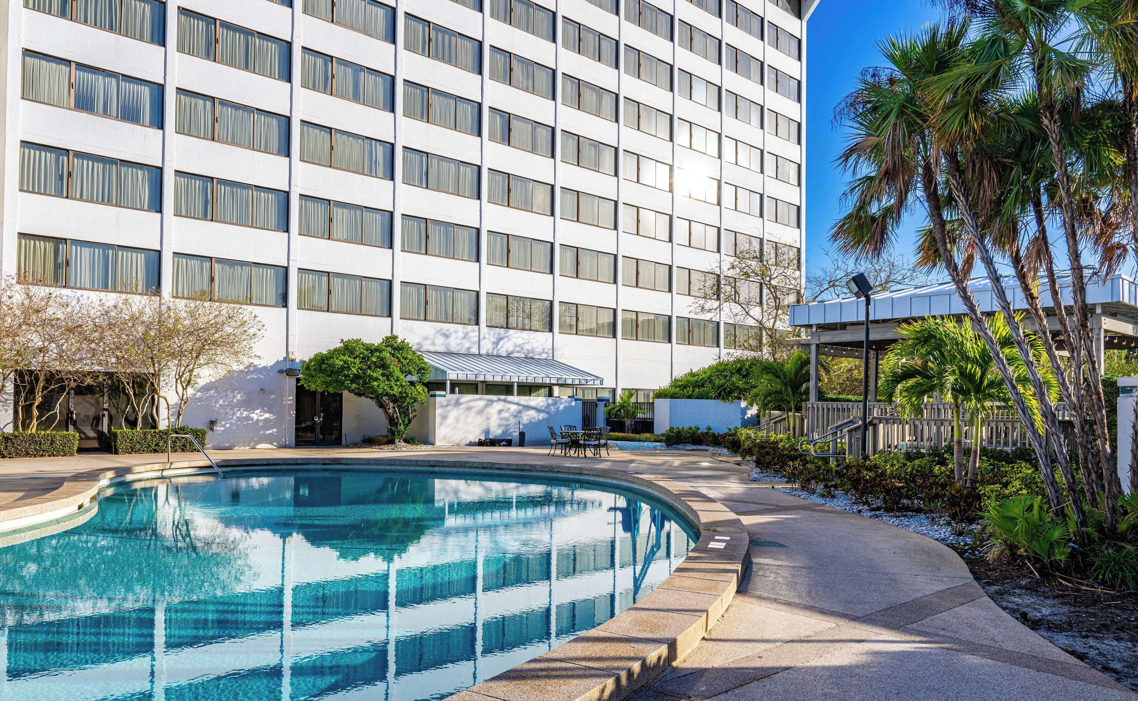 Un hotel moderno con una piscina grande, palmeras y un cielo azul despejado.