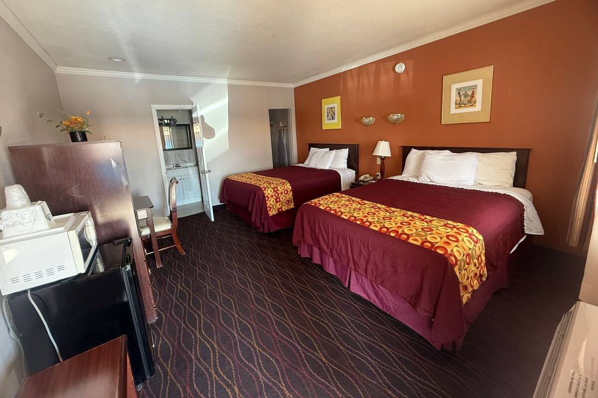 A hotel room with two beds, a desk, a chair, a mirror, a wardrobe, and a bathroom door.