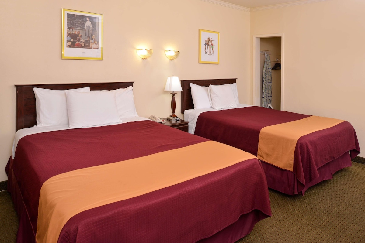 Een hotelkamer met twee bedden, een nachtkastje met een lamp en twee wandlampen.