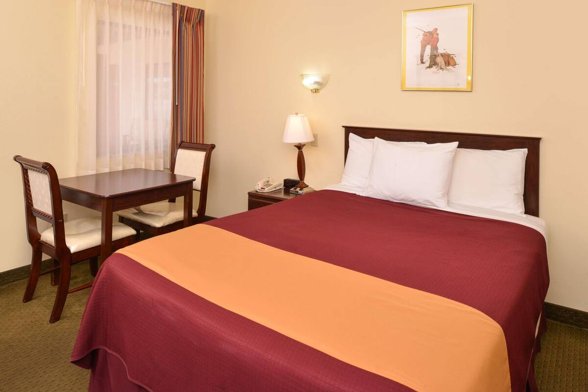 A hotel room with a bed, a desk, a chair, a lamp, and a framed picture on the wall.