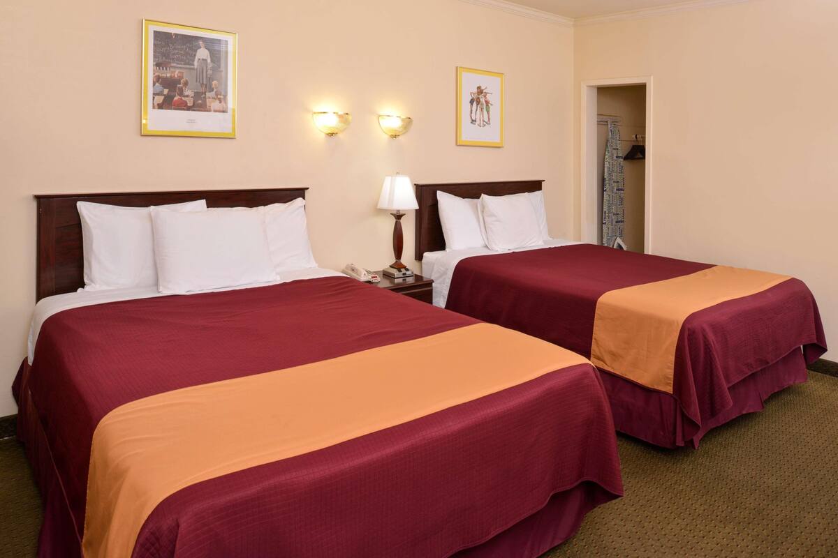 A hotel room with two beds, a nightstand with a lamp, and two wall-mounted light fixtures.