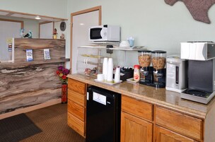 Una cocina equipada con microondas, cafetera y refrigerador. También hay tazas y un dispensador de café en la encimera.