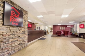 A Red Roof Inn reception area with a stone wall, a reception desk, a seating area with chairs, and a fireplace. - Red Roof Inn Winchester - Lexington East (Winchester)