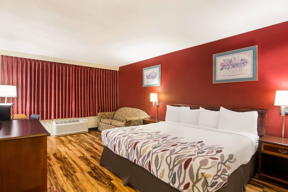 Ein Hotelzimmer mit einem großen Bett, einem Schreibtisch, einem Sessel und zwei Wandlampen.