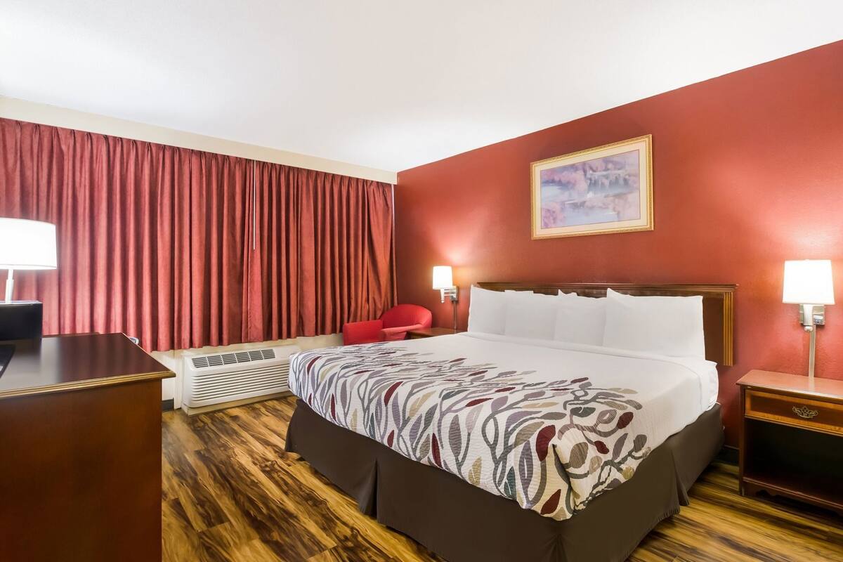 Ein Hotelzimmer mit Bett, Schreibtisch, Stuhl, Heizung und einem Bild an der Wand.