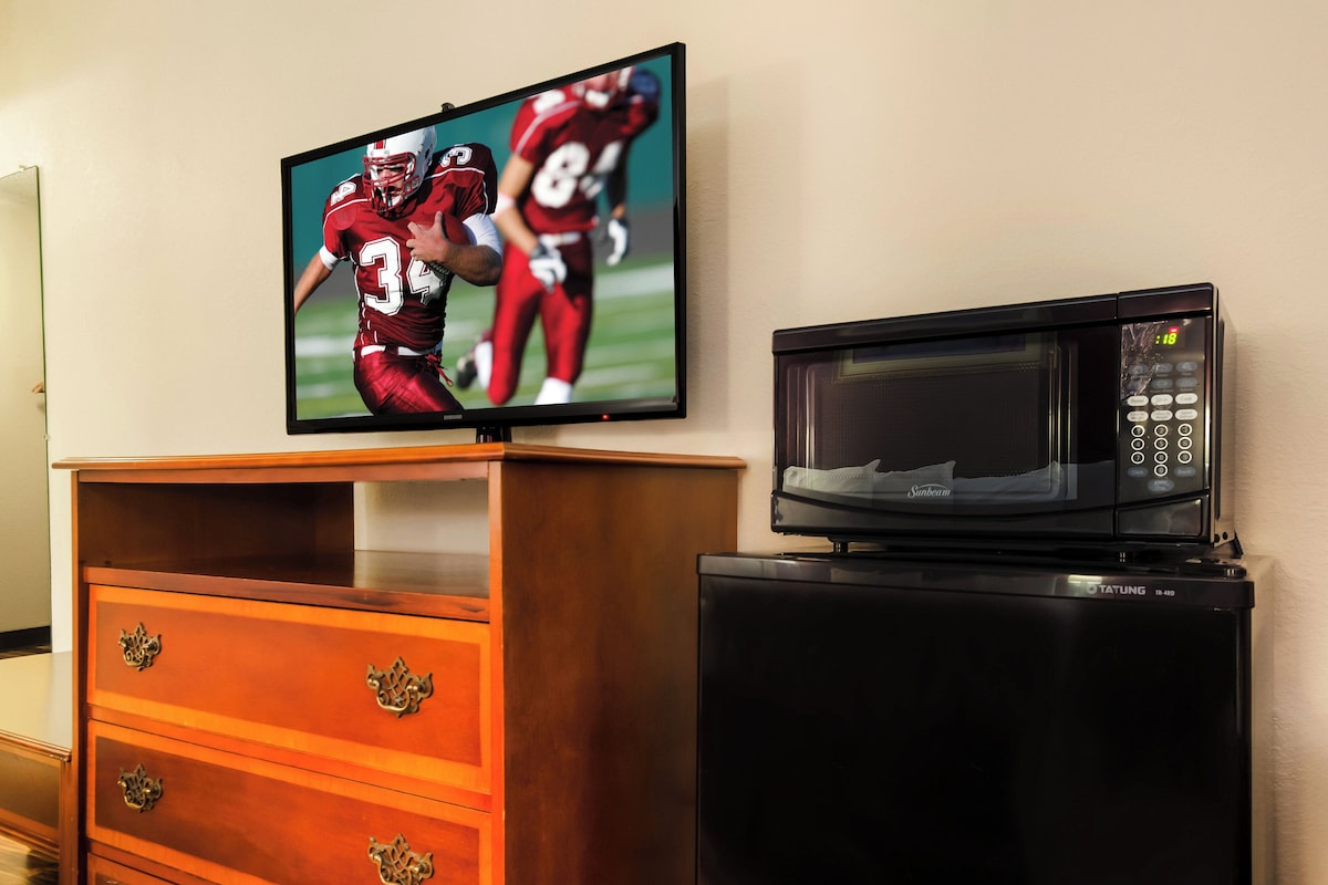 A television mounted on a wooden dresser with drawers, and a microwave oven on top of a black cabinet.