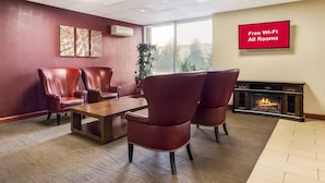 A modern lounge area with leather chairs, a wooden coffee table, and a fireplace. A sign indicates free Wi-Fi is available in all rooms. - Red Roof Inn Winchester - Lexington East (Winchester)