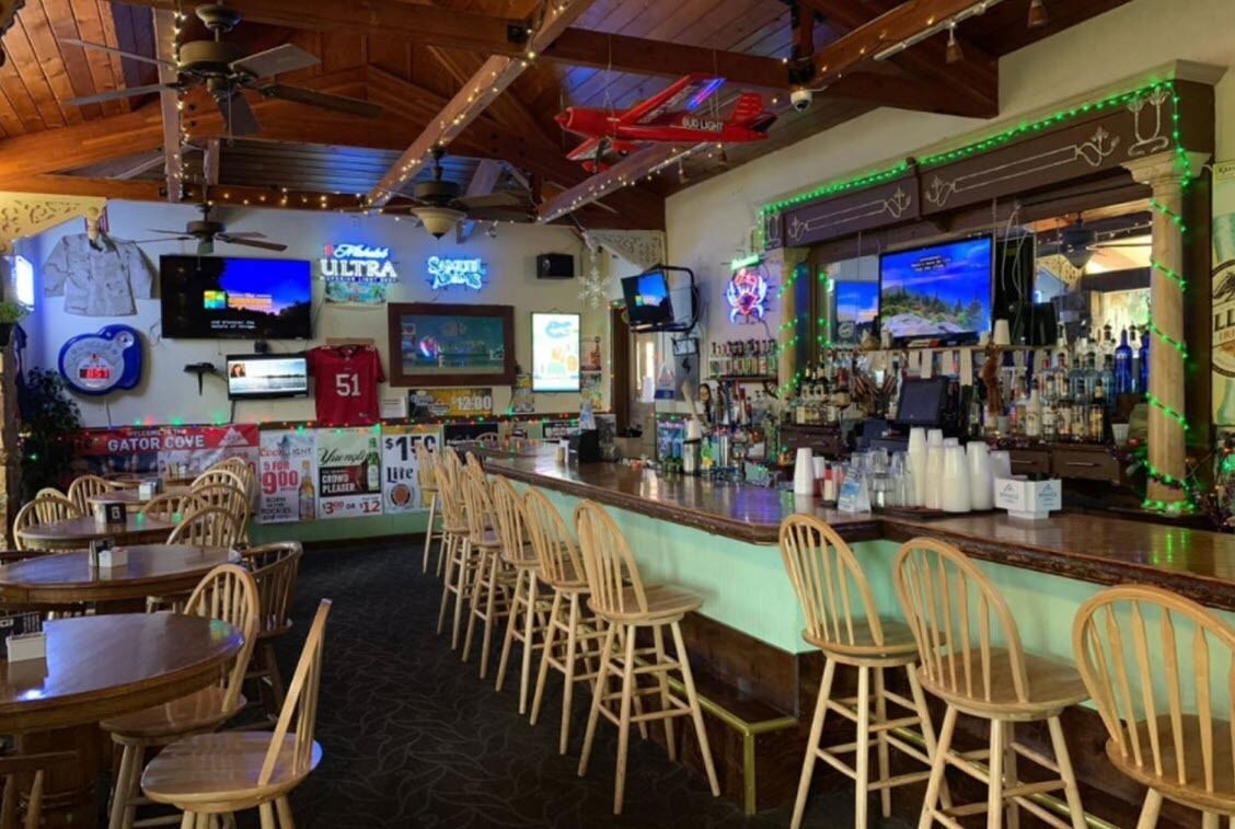 Zona de bar con sillas de madera, una barra con botellas y luces de neón.