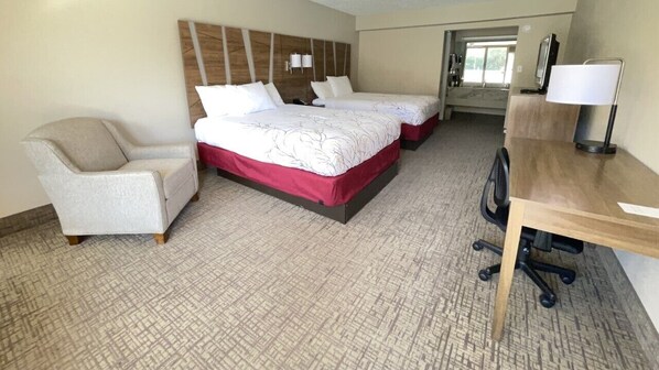 A hotel room with two beds, a desk, a chair, and a large window.