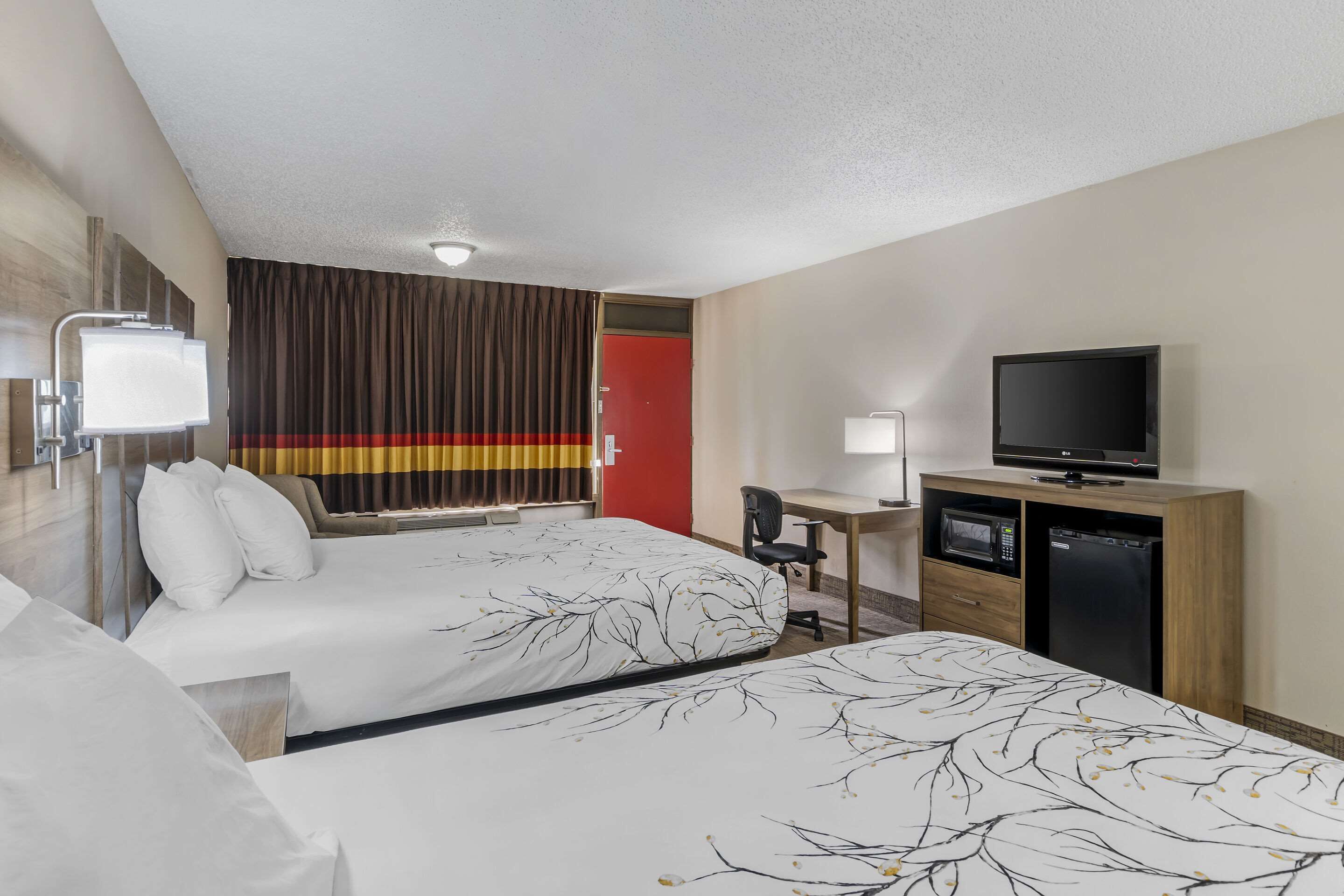 A hotel room with two beds, a desk with a chair, a television, a microwave, and a refrigerator.
